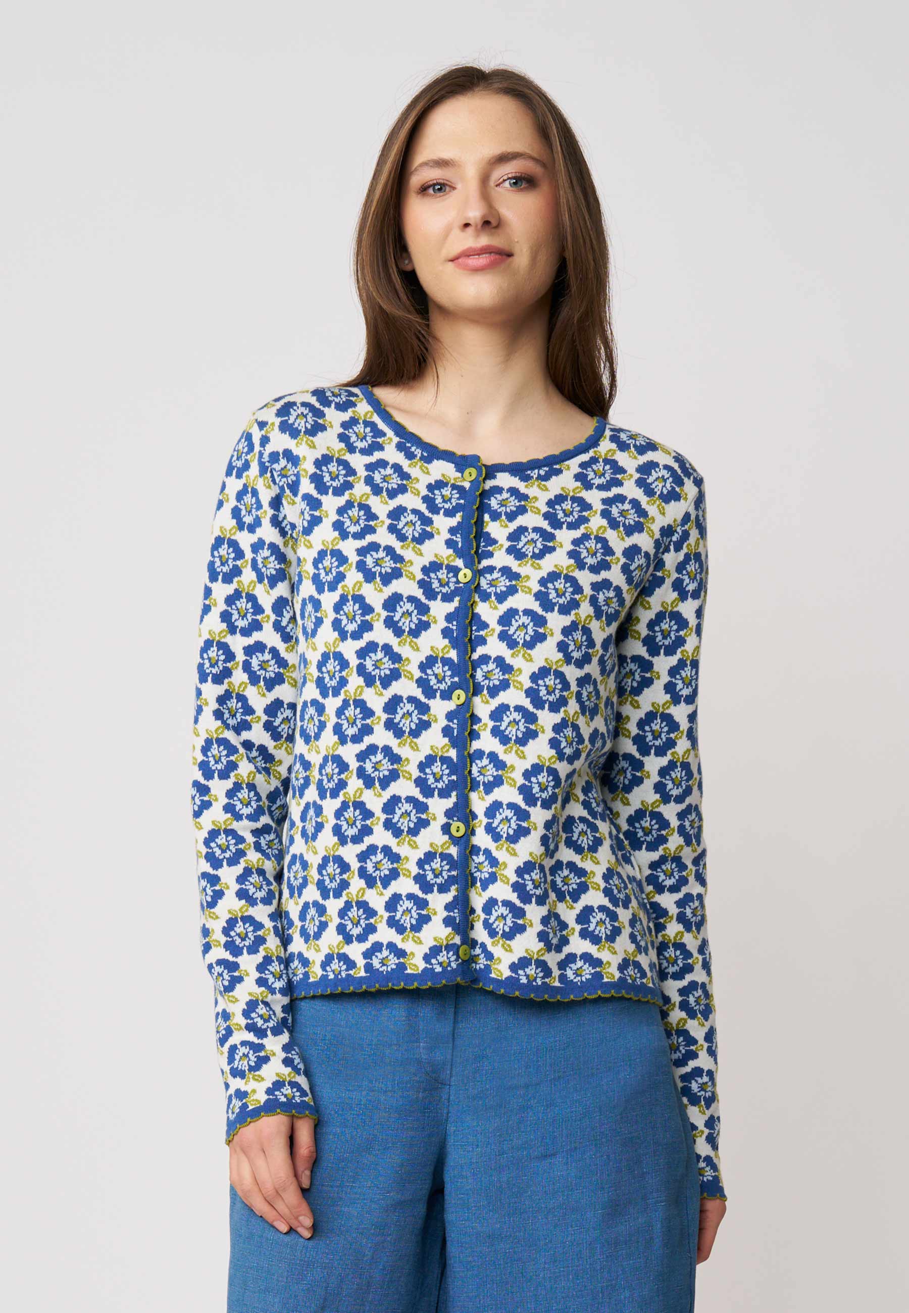 Frau trägt Strickjacke, Modell Juliana, mit blauem Blumenmuster auf weißem Grund vor hellem Hintergrund