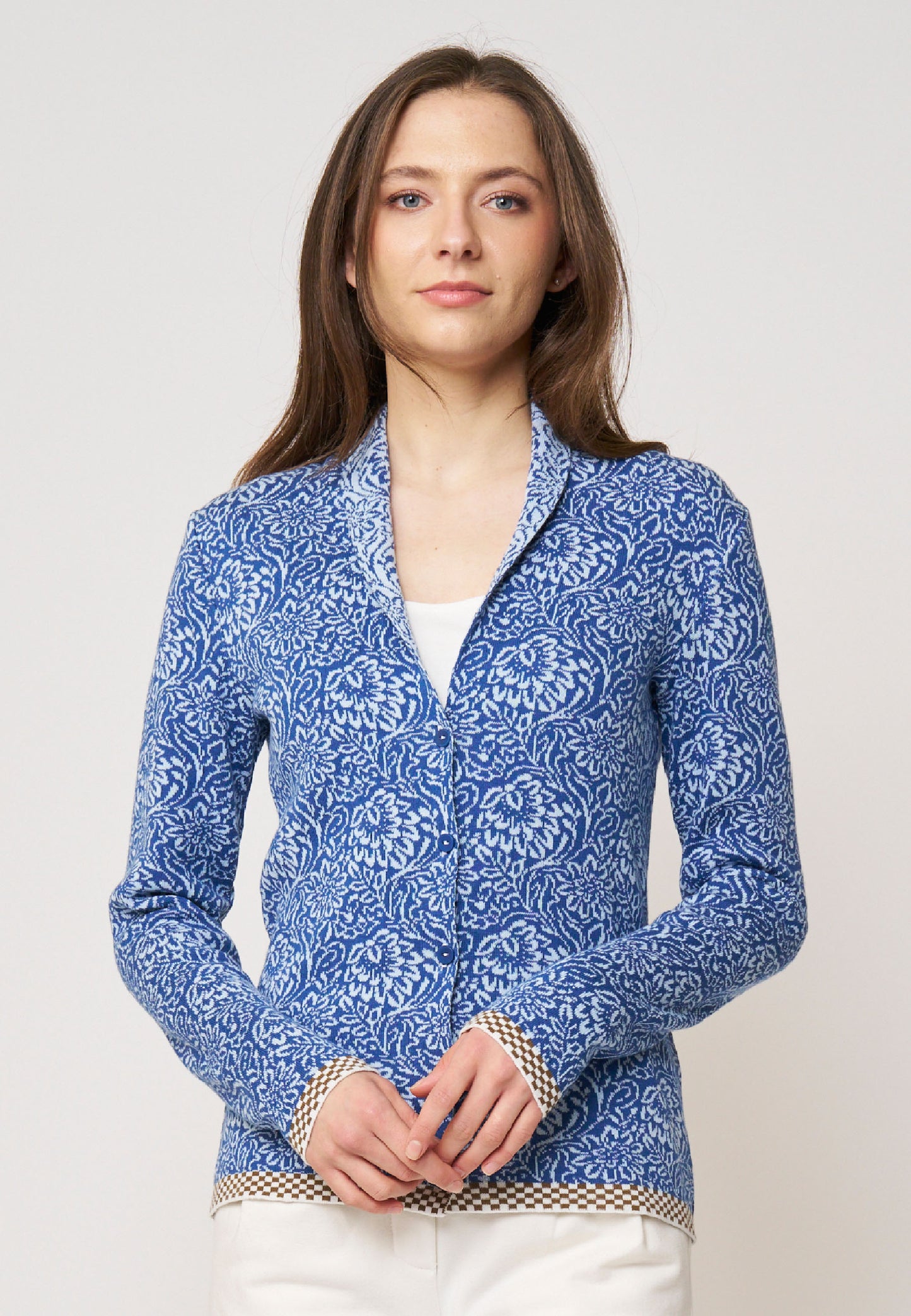 Frau präsentiert Strickjacke, Modell Jolie, in Blau mit floralem Muster und kontrastierendem Saum in Beige-Weiß, frontal