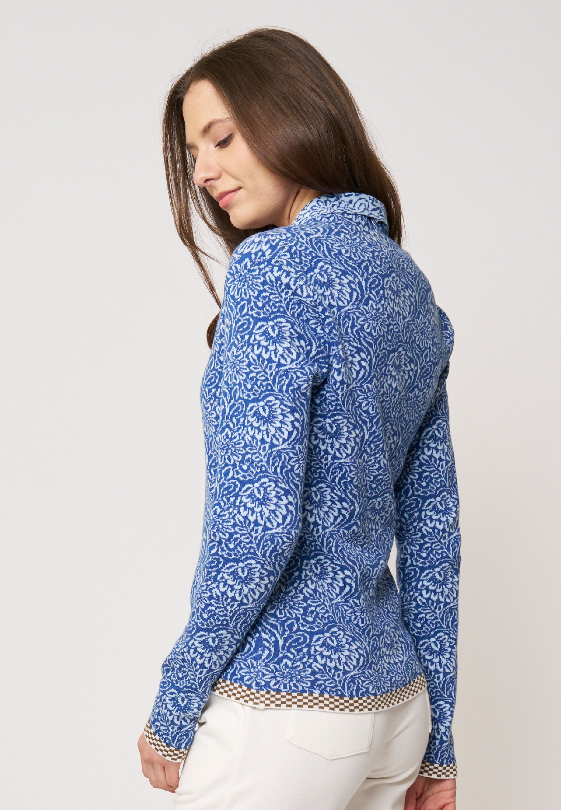 Frau zeigt Strickjacke, Modell Jolie, in Blau mit feinem floralen Muster und kontrastierendem Saum in Braunweiß, Rückansicht