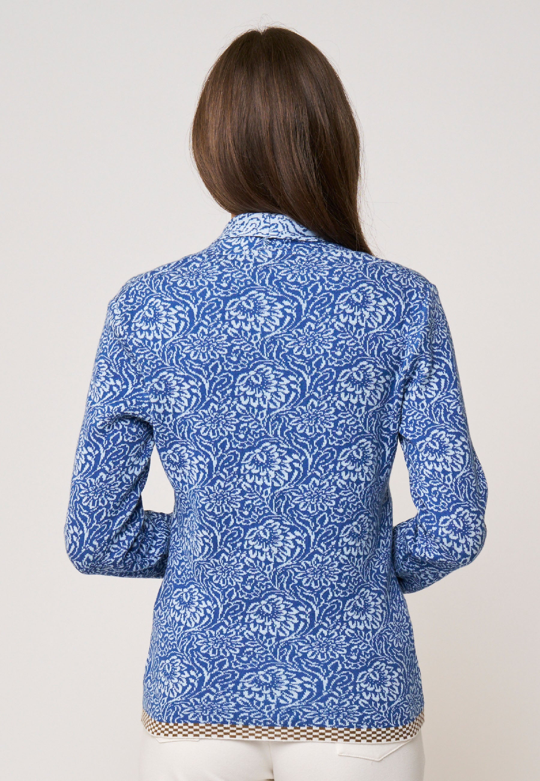 Frau trägt Strickjacke, Modell Jolie, mit weiß-blauem floralen Muster und langem Arm vor hellgrauem Hintergrund