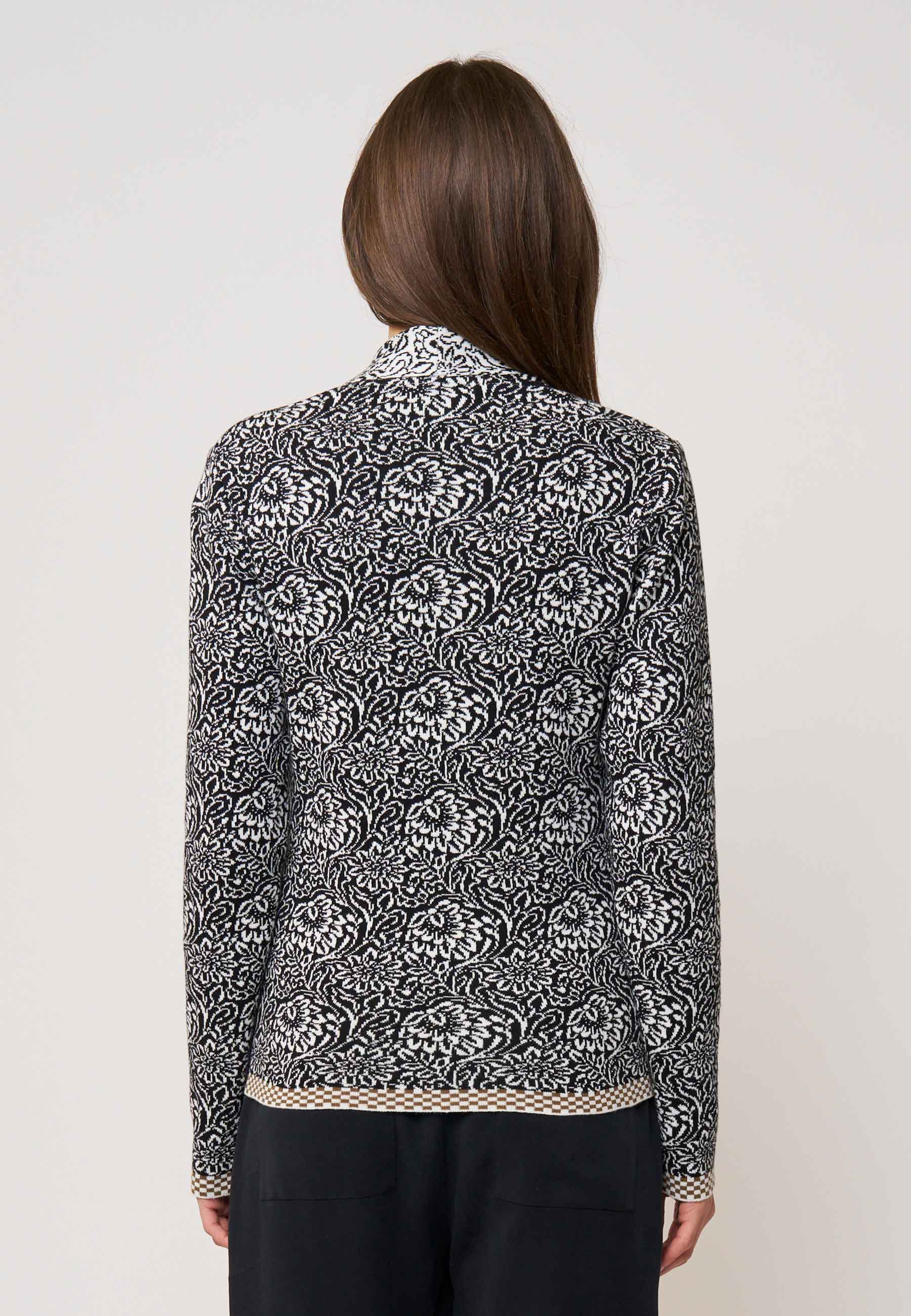 Frau trägt Strickjacke, Modell Jolie, in Schwarz mit weißem floralem Muster, Rückansicht, leichter Saumabschluss