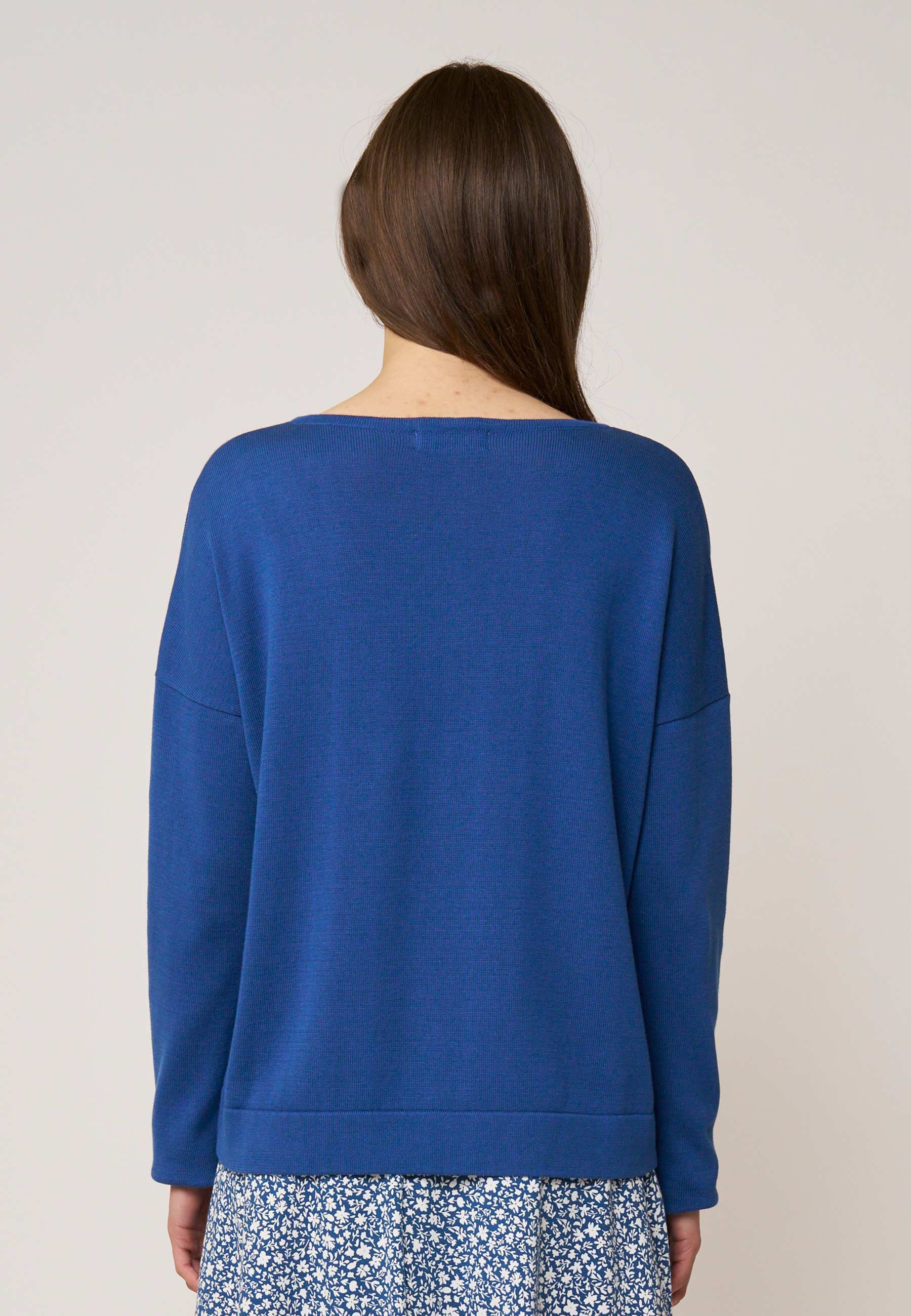 Frau mit braunem langen Haar trägt locker sitzenden, unifarbenen blaugrünen Pullover mit geradem Schnitt von hinten betrachtet