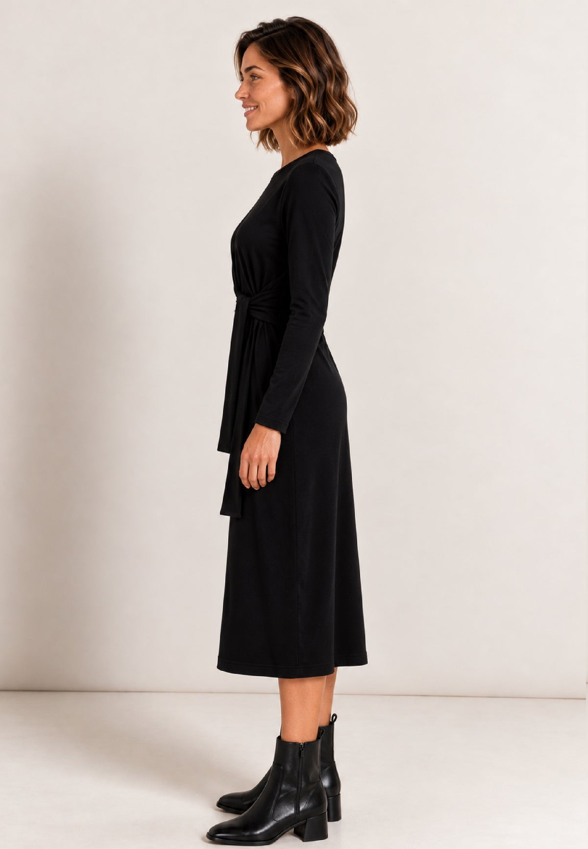 Kleid, Modell June in Schwarz an Frau im Profil mit schwarzen Stiefeletten vor hellem Hintergrund