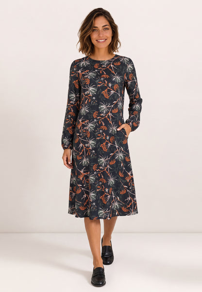 Kleid, Modell Isolde mit floralem Muster an lächelnder Frau mit schwarzen Loafern