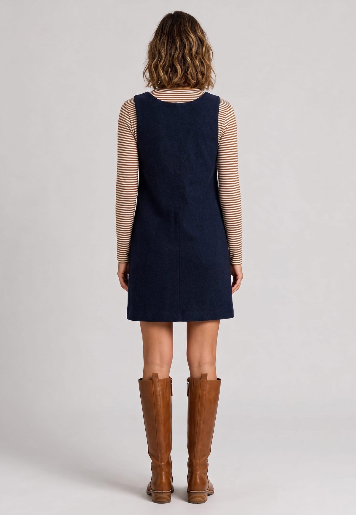 Trägerkleid, Modell Liza von hinten über gestreiftem Langarmshirt mit braunen Stiefeln vor grauem Hintergrund