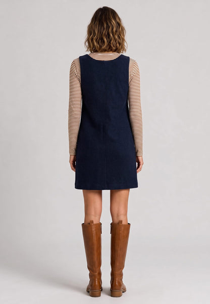 Trägerkleid, Modell Liza von hinten über gestreiftem Langarmshirt mit braunen Stiefeln vor grauem Hintergrund