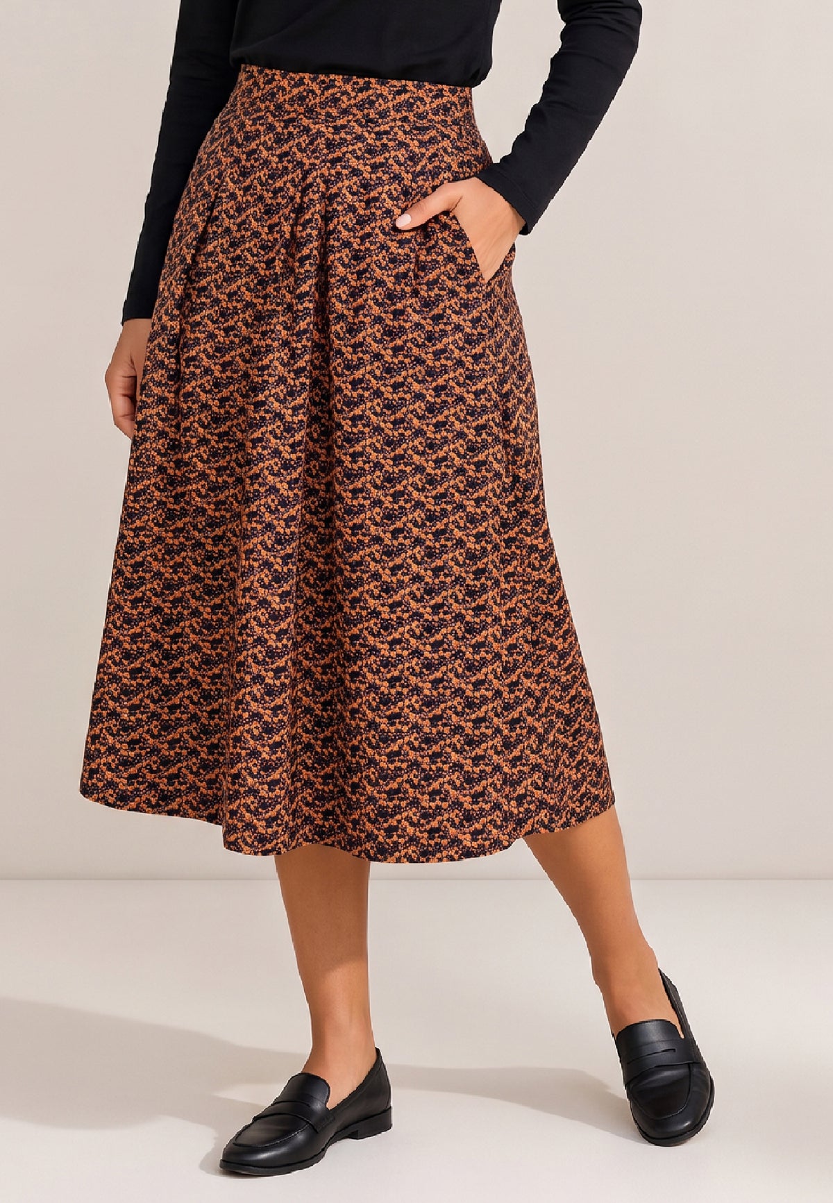 Frau trägt Rock, Modell Elsa, mit orange-schwarzem Muster, Taschen und schwarzen Loafern