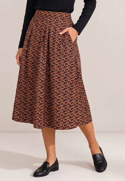 Frau trägt Rock, Modell Elsa, mit orange-schwarzem Muster, Taschen und schwarzen Loafern