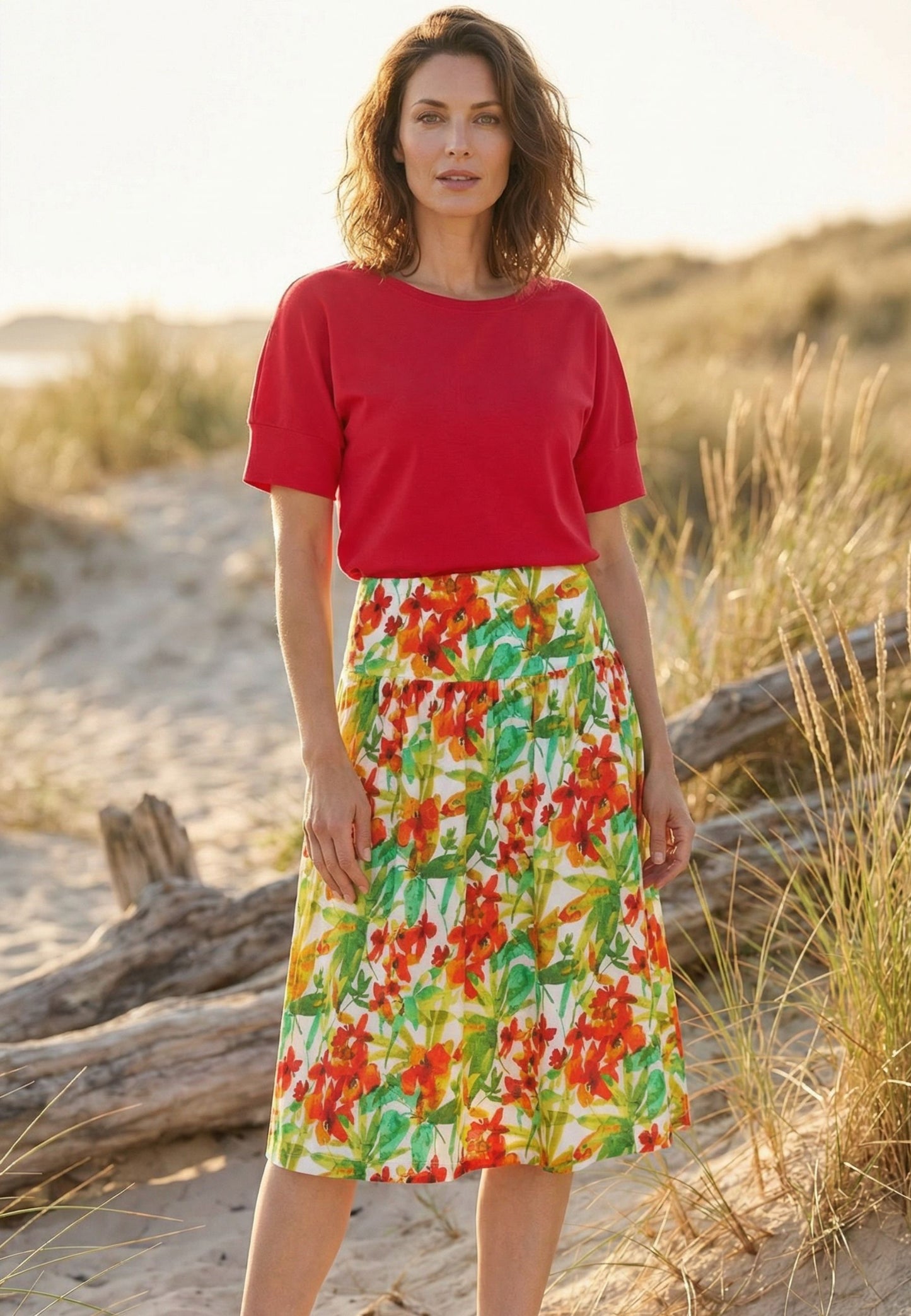 Rock, Modell Donia mit farbenfrohem Blumenmuster in Rot- und Grüntönen, midi-lang, getragen von stehendem Model am Strand
