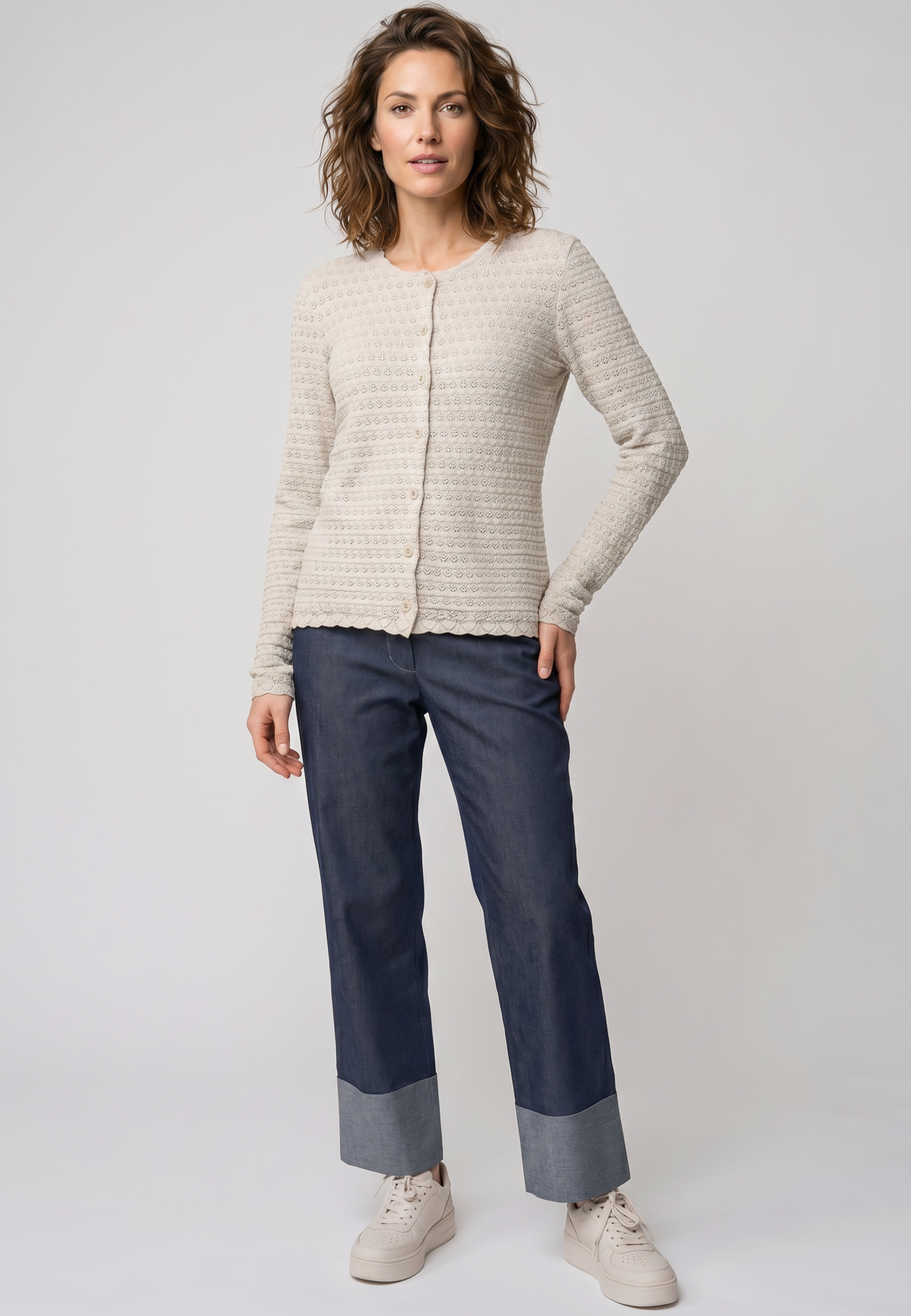 Strickjacke, Modell Marcelina in cremeweiß mit feinem Muster und Knopfleiste, langärmelig, stehend vor heller Kulisse