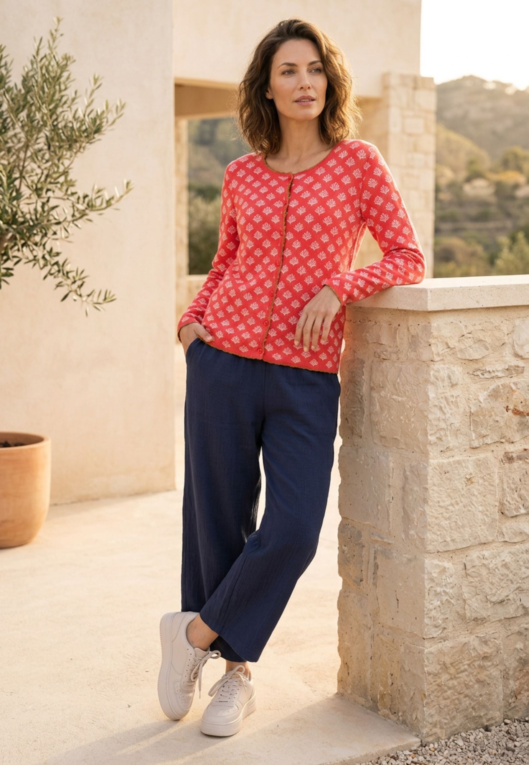 Strickjacke, Modell Lena in Koralle mit zartem Muster, langärmelig, frontale Ansicht getragen in sommerlicher Umgebung