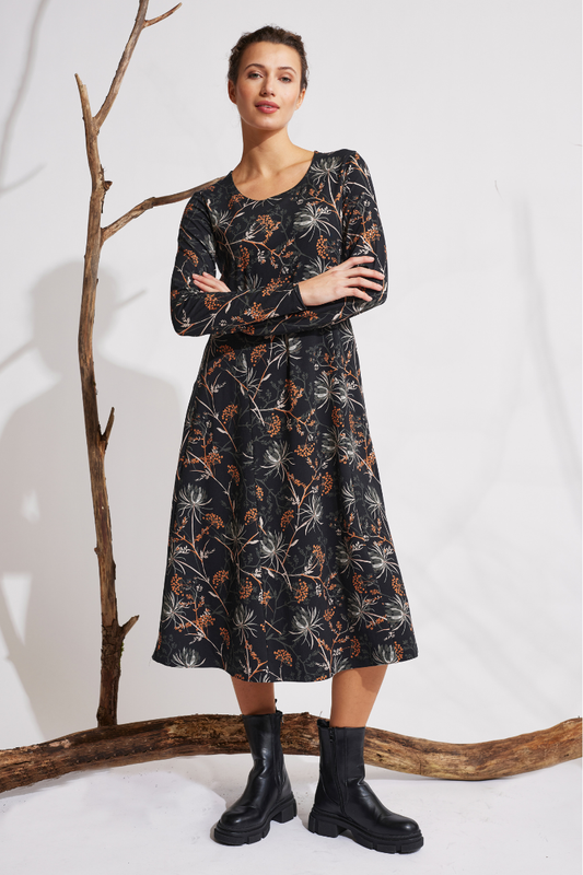 Frau trägt langärmliges Kleid, Modell Rana mit floralen Mustern in Orange und Weiß vor hellem Hintergrund
