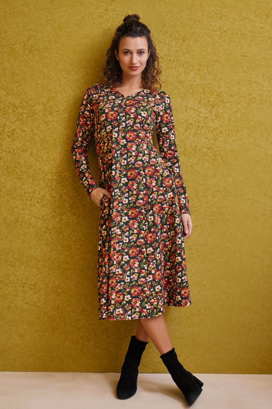 Frau trägt Kleid, Modell Avalon mit langem Arm und buntem Blumenmuster vor goldgelbem Hintergrund